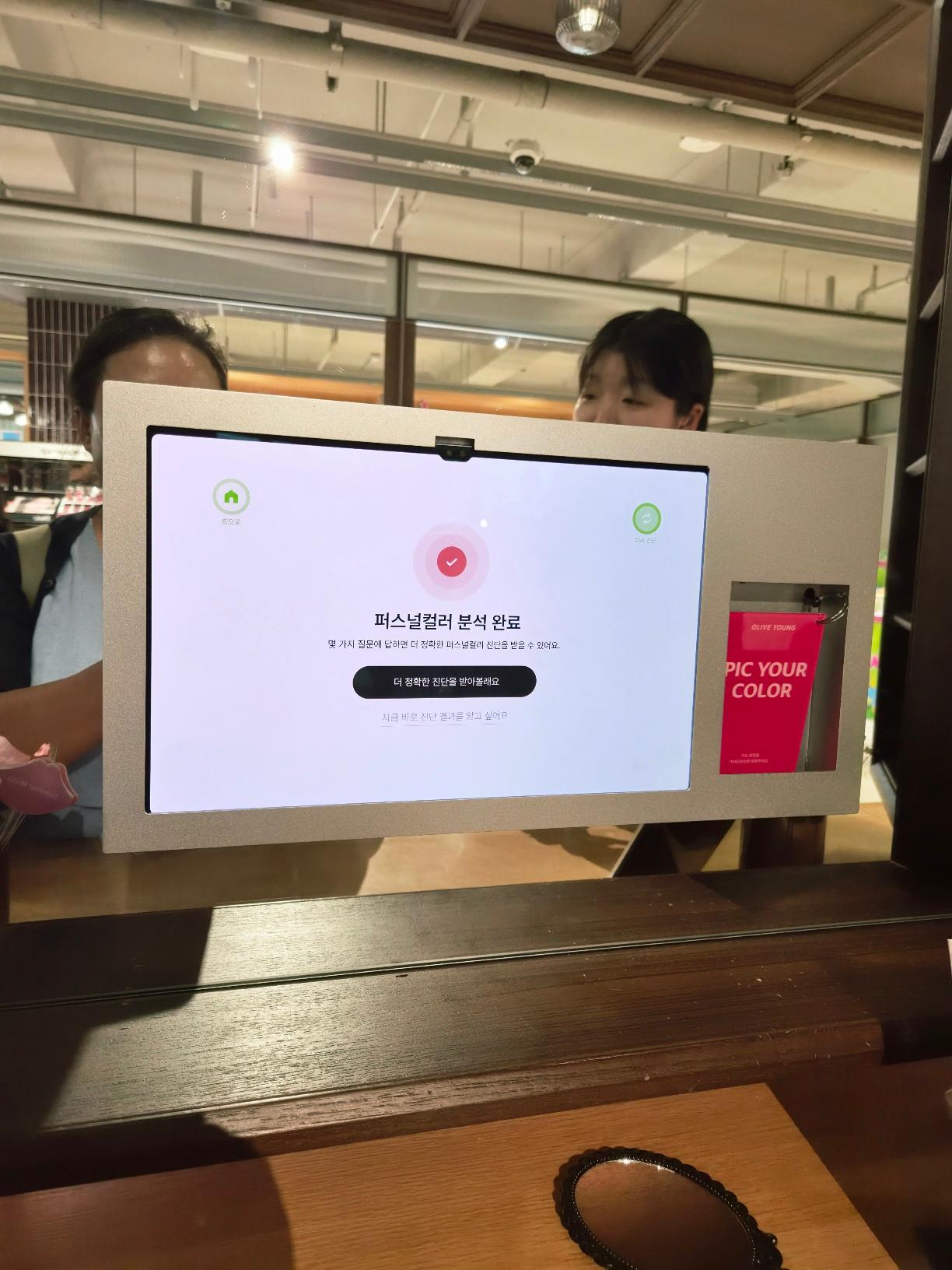 The kiosk screen showing a completion checkmark and a button to proceed with the detailed skin tone report.