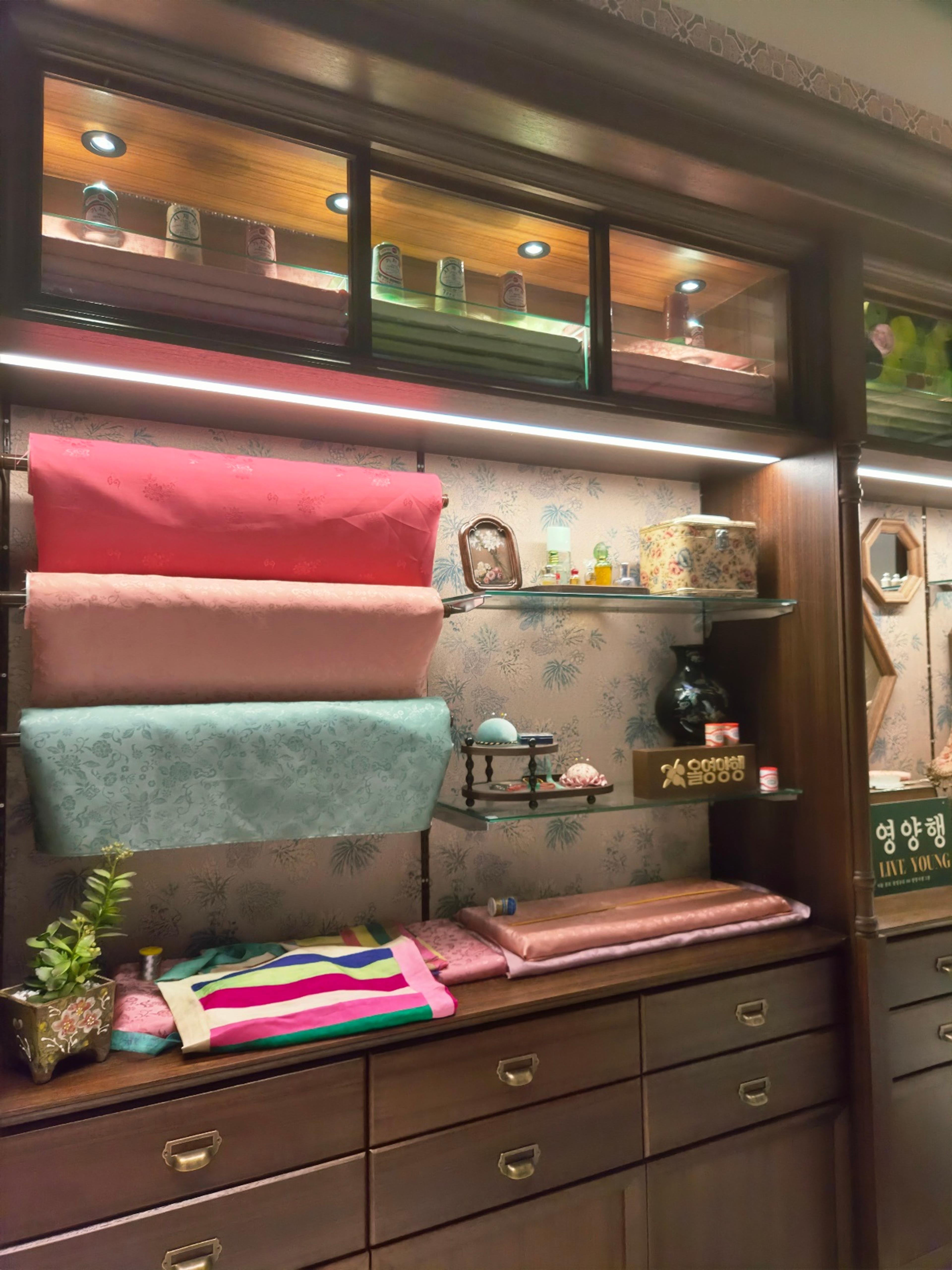 A wide view of a wooden cabinet display with rolls of premium silk fabrics and vintage apothecary jars on glass shelves.