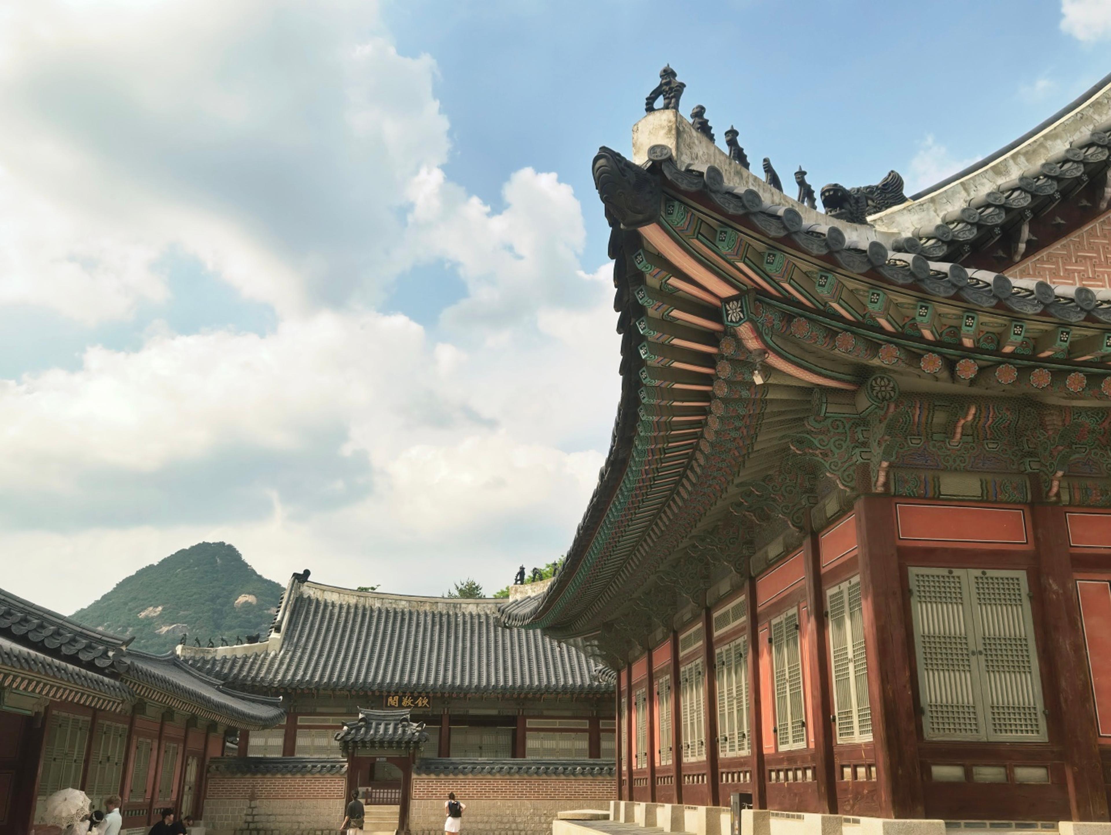 Close-up of Gyeongbokgung Palace roof corner with vibrantly painted dancheong wooden beams in green, orange, blue, and yellow against a cloudy sky