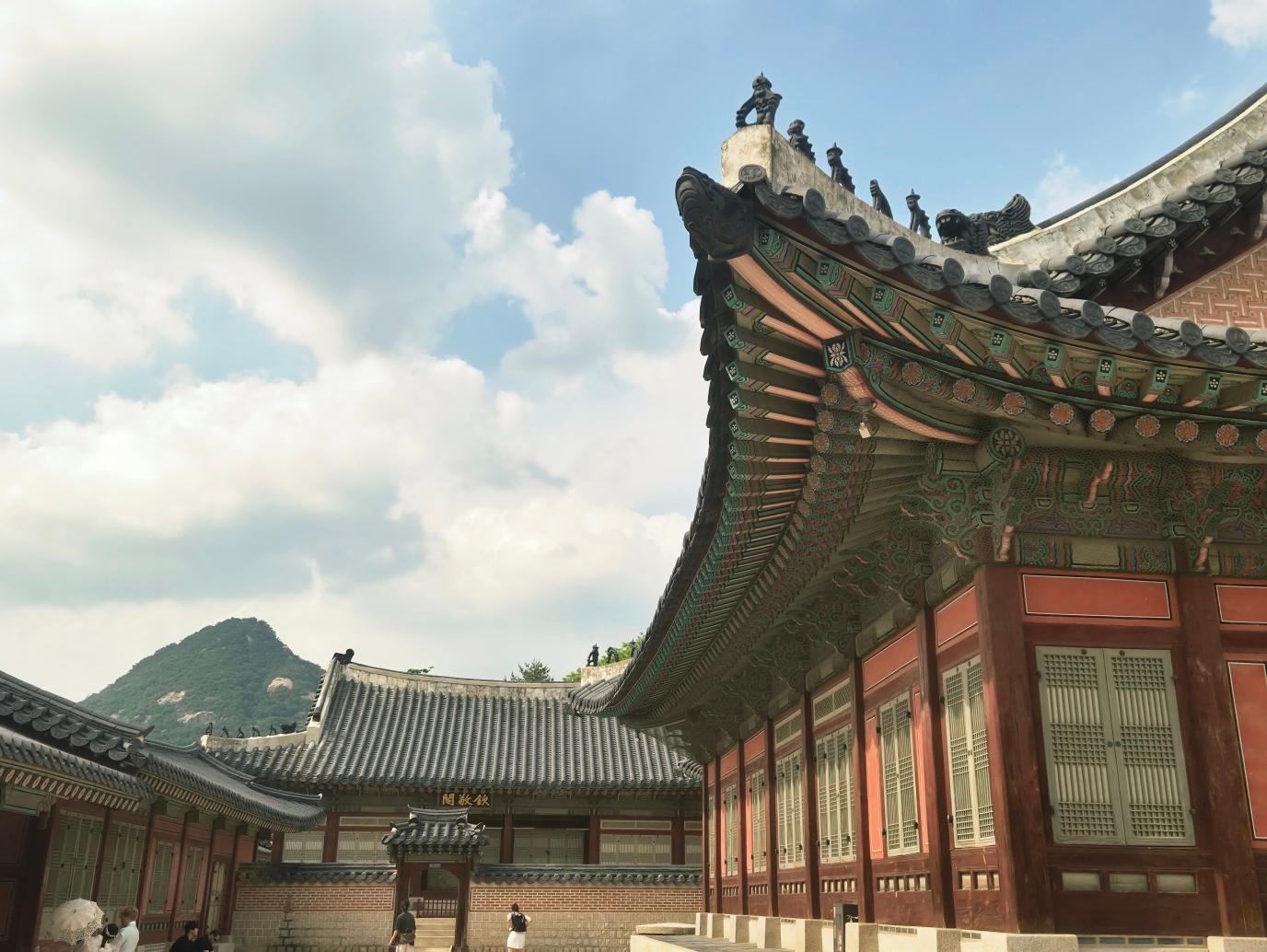 Close-up of Gyeongbokgung Palace roof corner with vibrantly painted dancheong wooden beams in green, orange, blue, and yellow against a cloudy sky