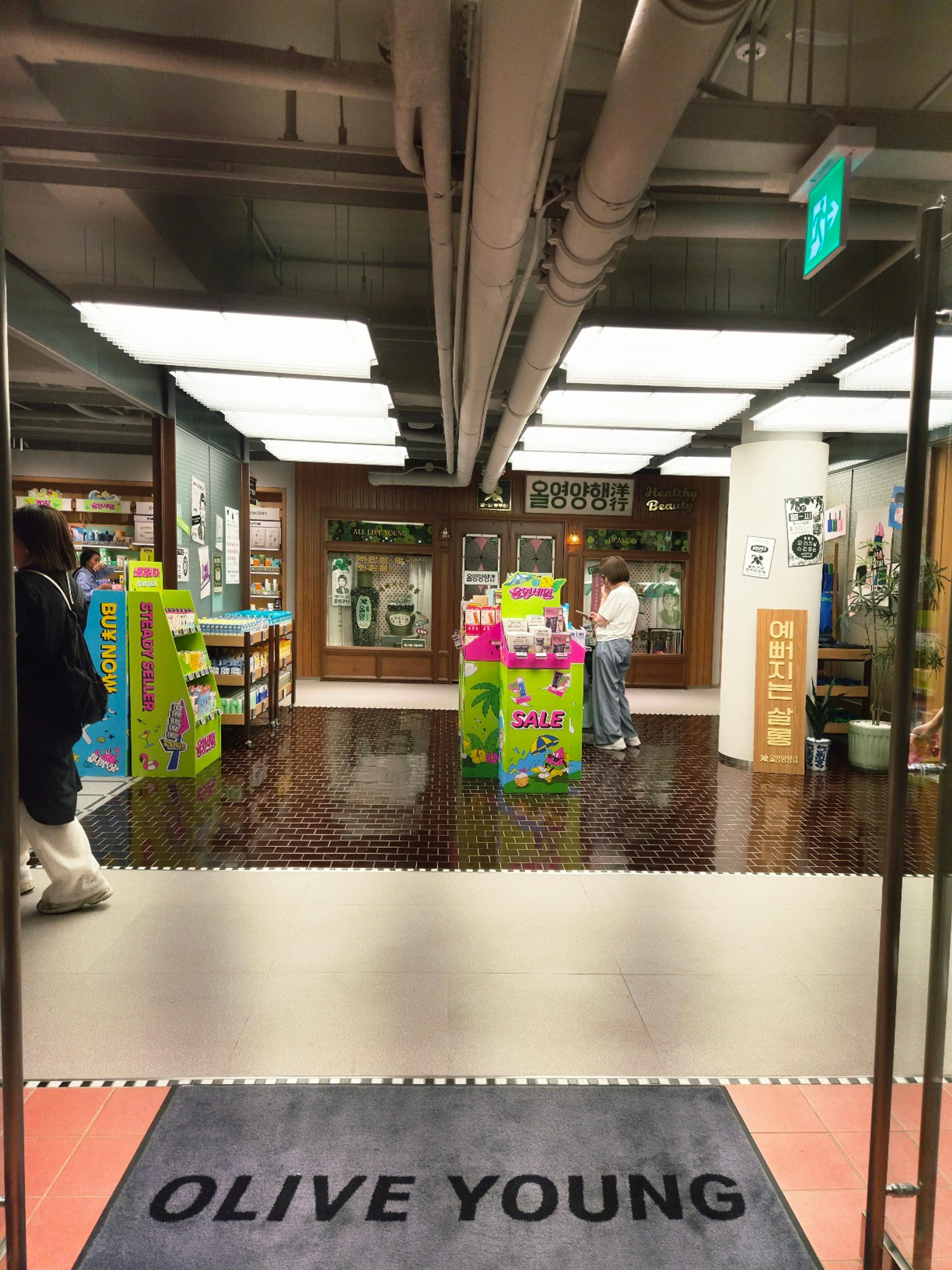 The main entrance view through glass doors revealing clean wooden product shelving and colorful promo towers inside.