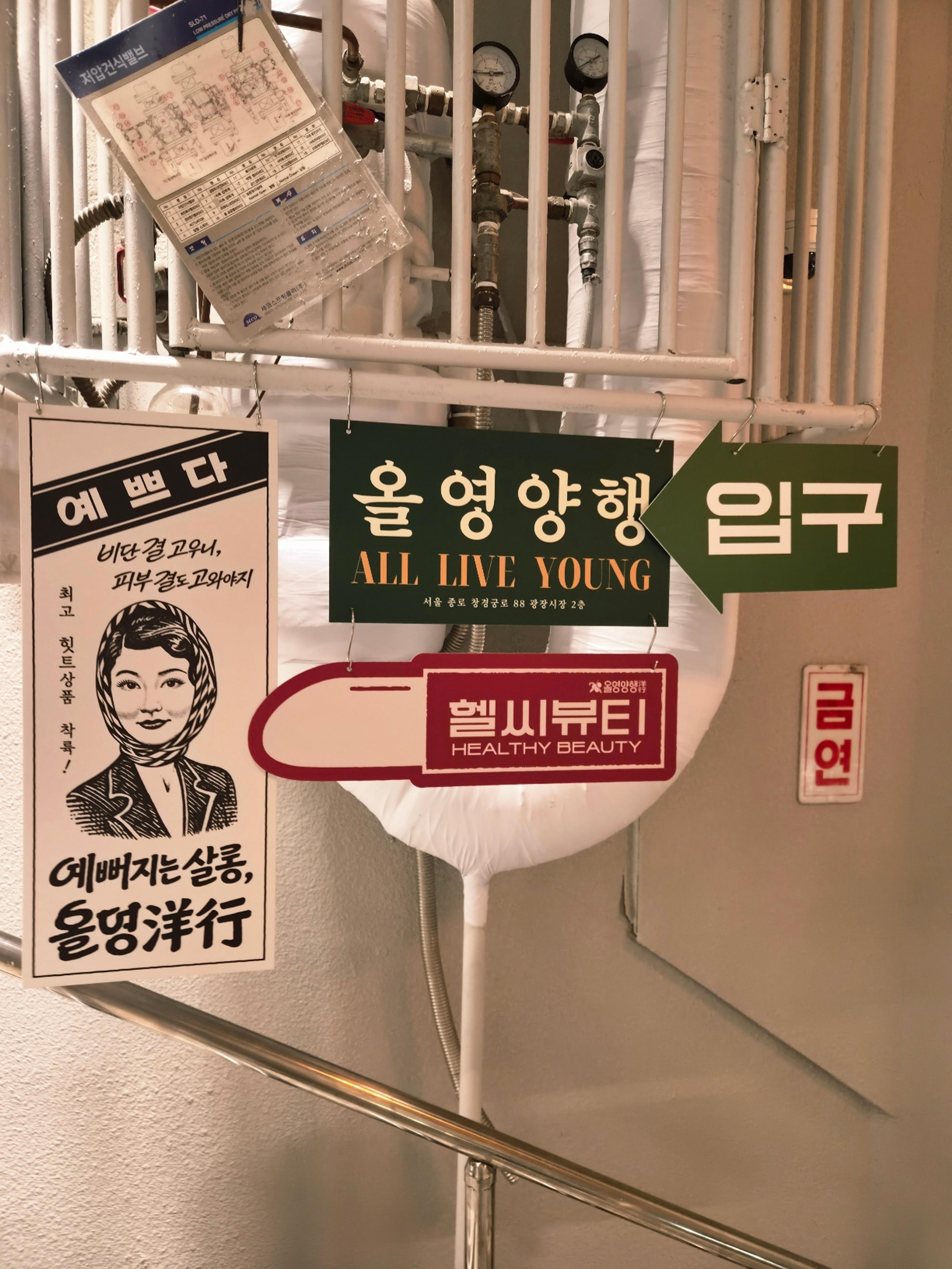 Vintage advertising banners and directional signs clipped onto industrial white pipes leading up the stairwell.