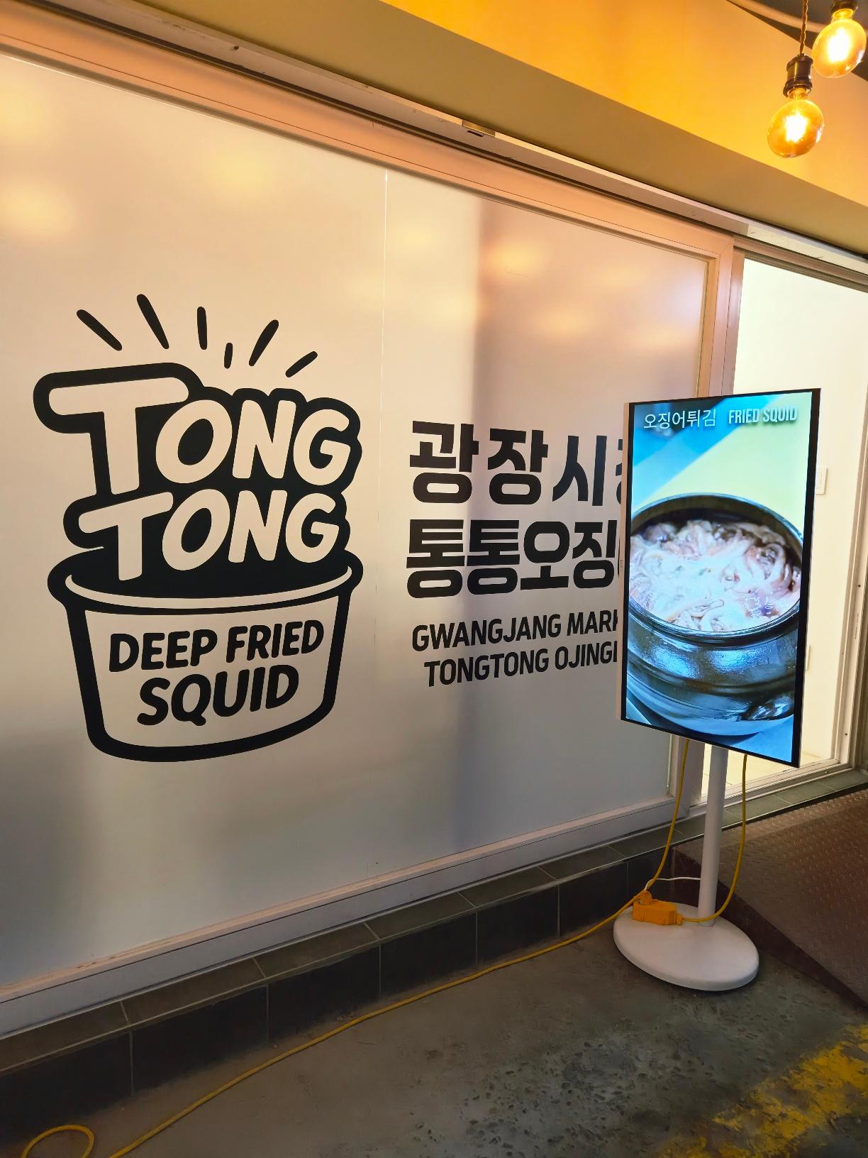 A minimalist frosted glass storefront for Tong Tong featuring a bold black logo that reads Tong Tong Deep Fried Squid.