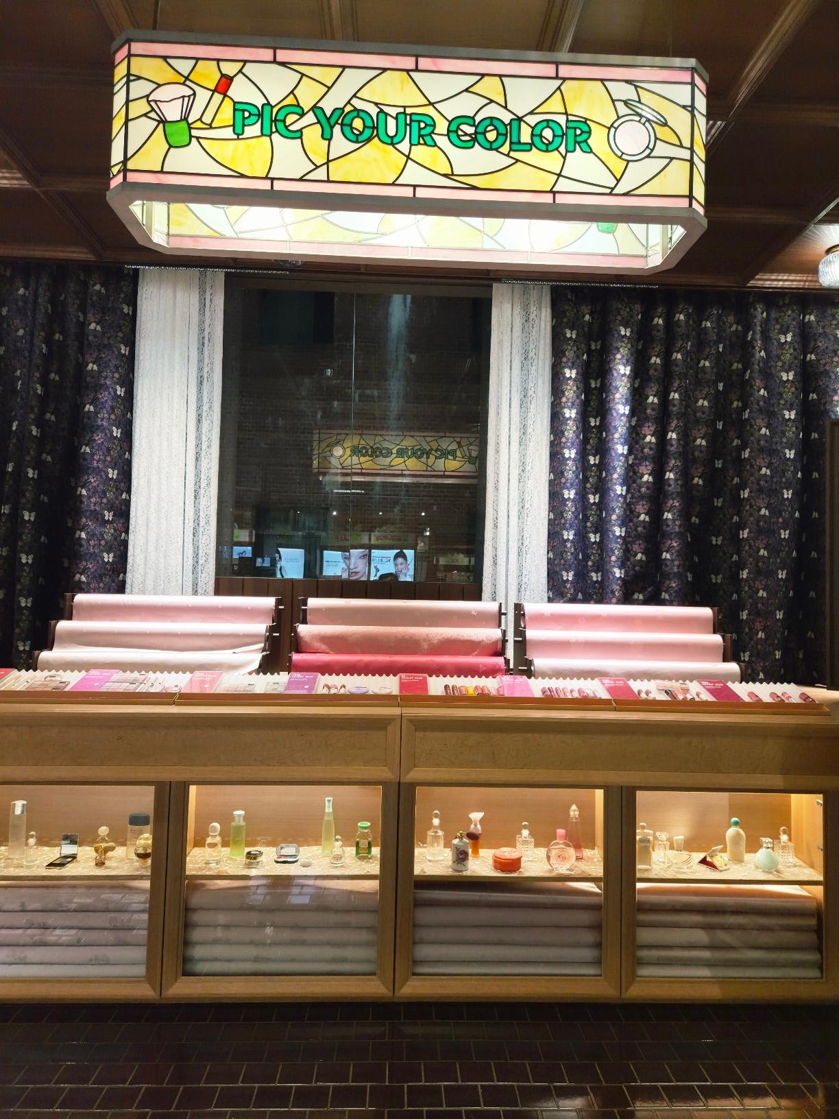 A beautifully framed perfume counter with an overhead stained glass sign reading Pic Your Color.
