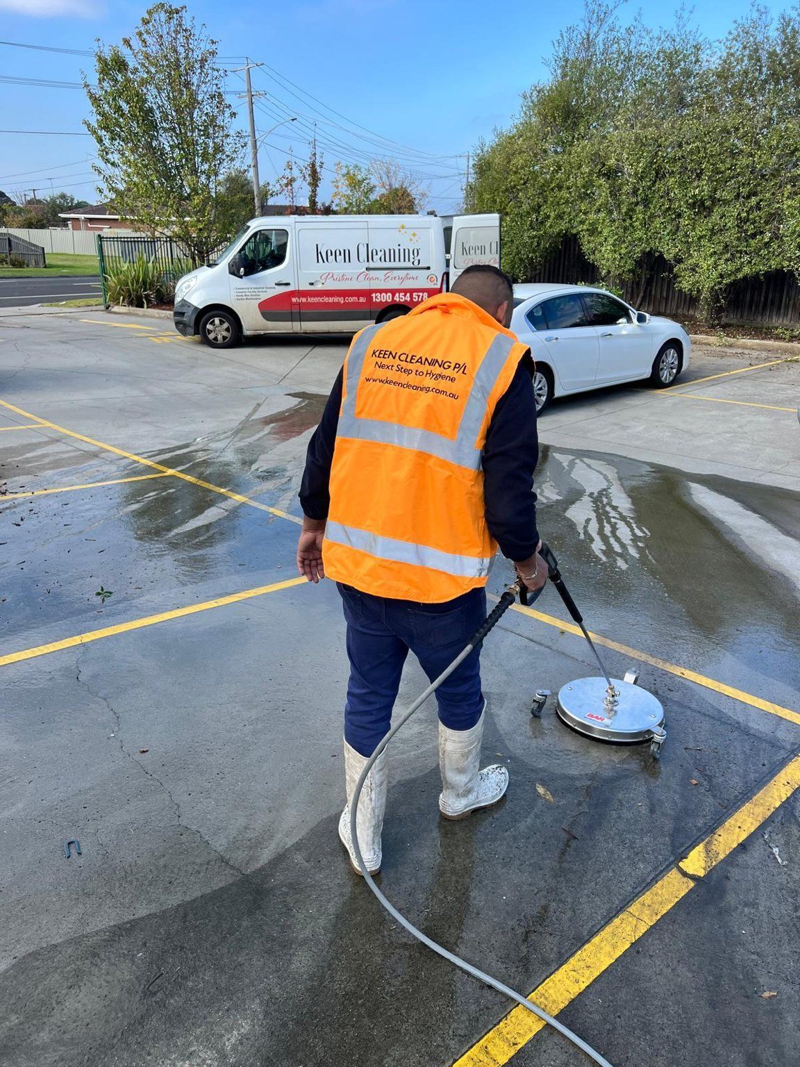 Keen Cleaning technician pressure-washing a car park with the branded van behind