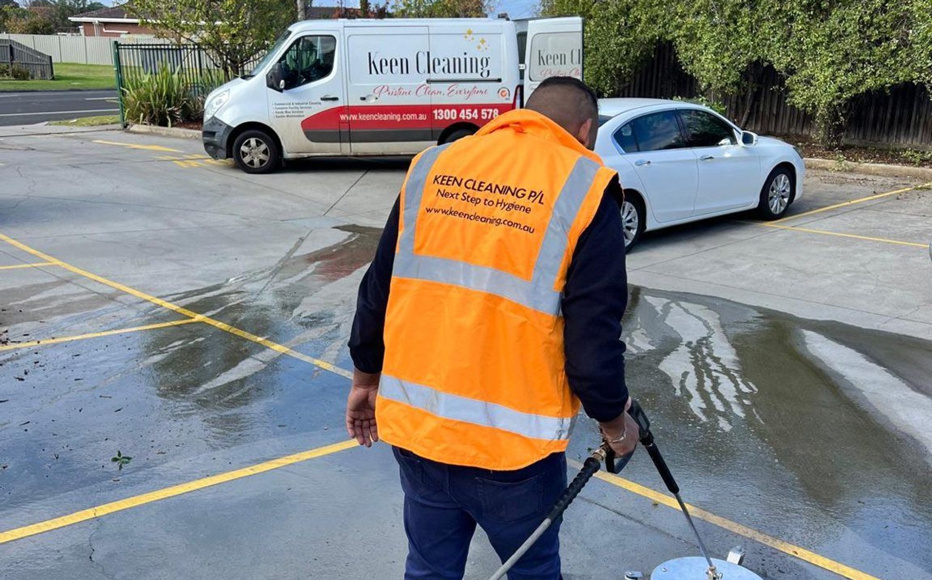 Keen Cleaning technician pressure-washing a car park with the branded van behind