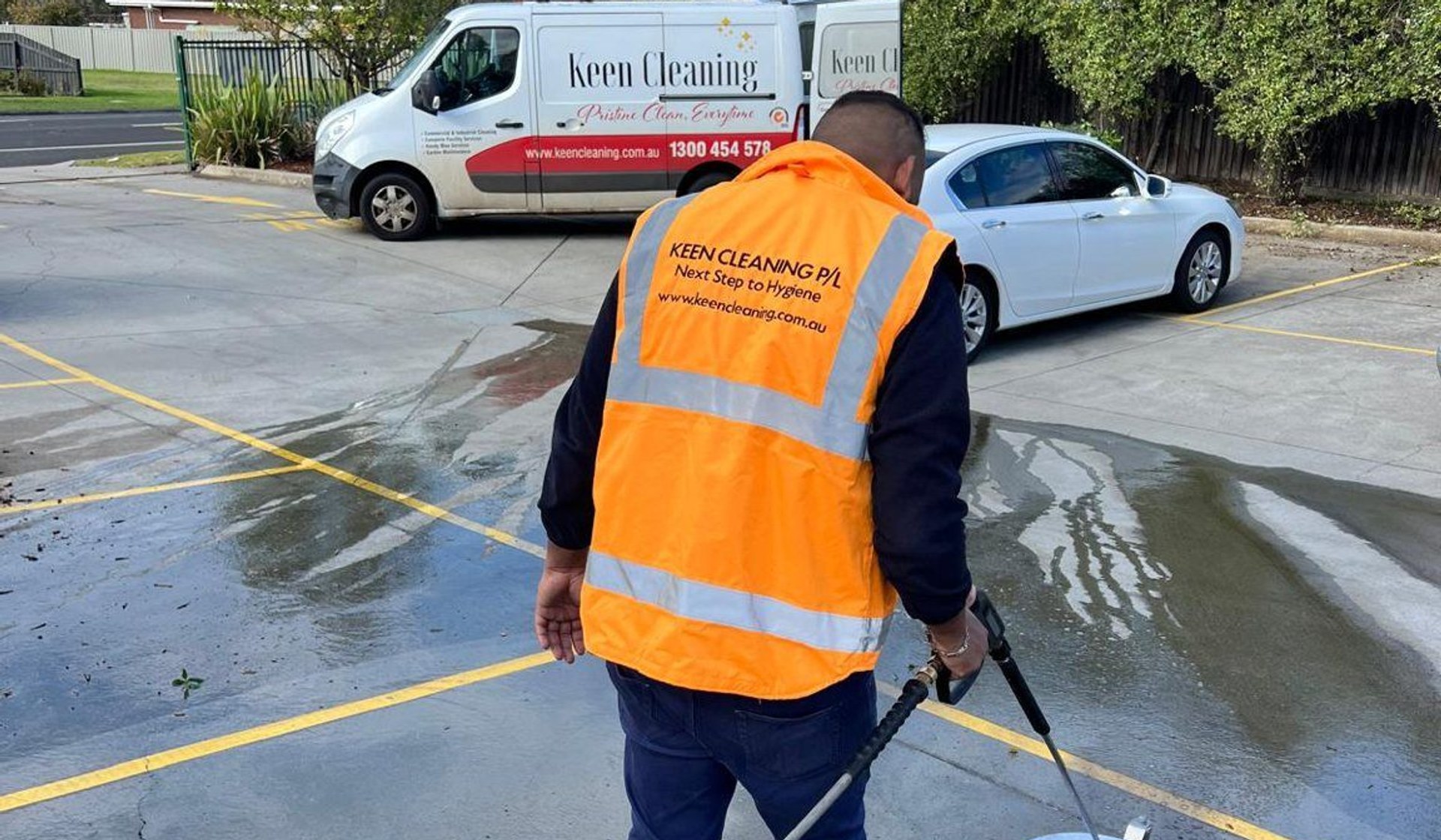 Keen Cleaning technician pressure-washing a car park with the branded van behind