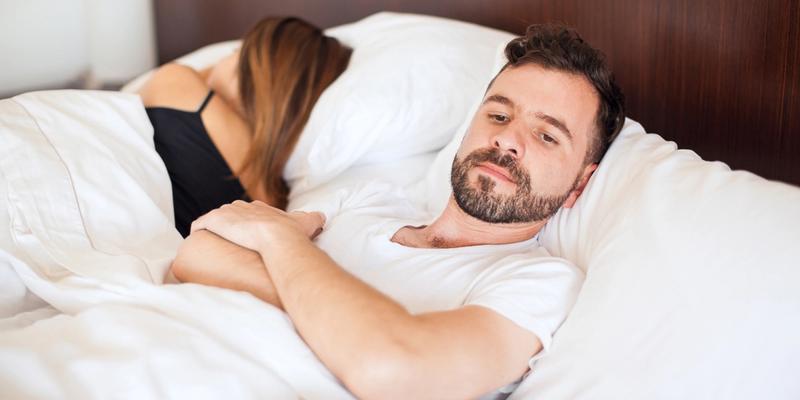 Mand med lav sexlyst, ligger i sengen med ryggen mod sin partner