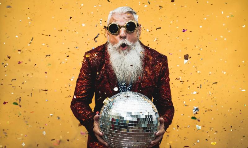 En festlig äldre man med vitt skägg som håller i en discokula. 