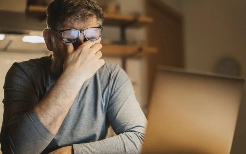 Træt mand i overgangsalderen gnider sig i øjnene foran en computer