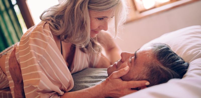Et midaldrende par ligger i sengen og kigger kærligt og flirtende på hinanden.