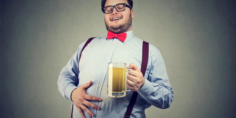 Glad man som håller i sin ölmage medan han dricker ett stort glas öl