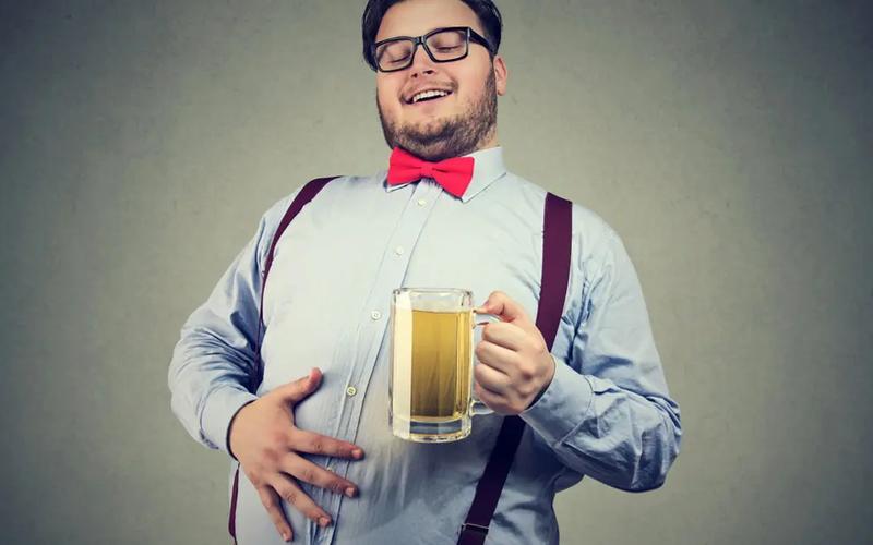 Glad mand som holder sig på sin ølmave mens han drikker et stort krus øl
