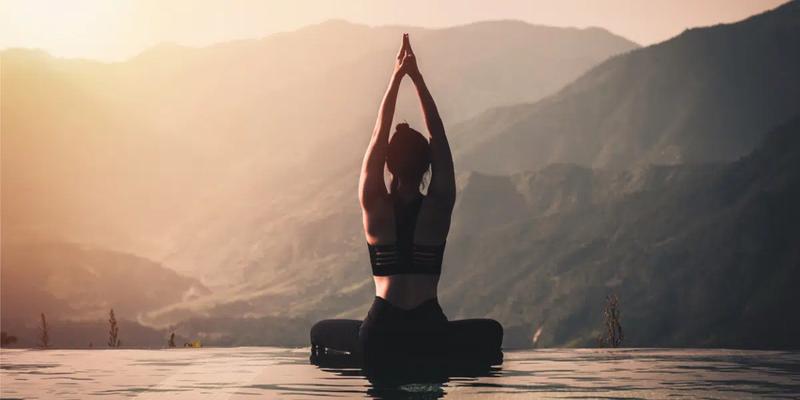 Kvinde i balancerende yogastilling med bjerge i baggrunden
