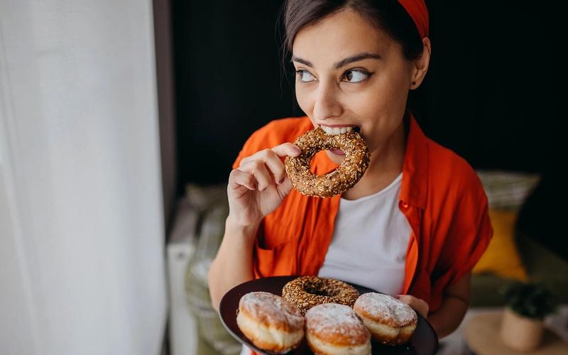Ung kvinne spiser donuts og berlinerboller