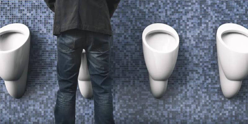 Mann står og urinerer ved en offentlig urinal