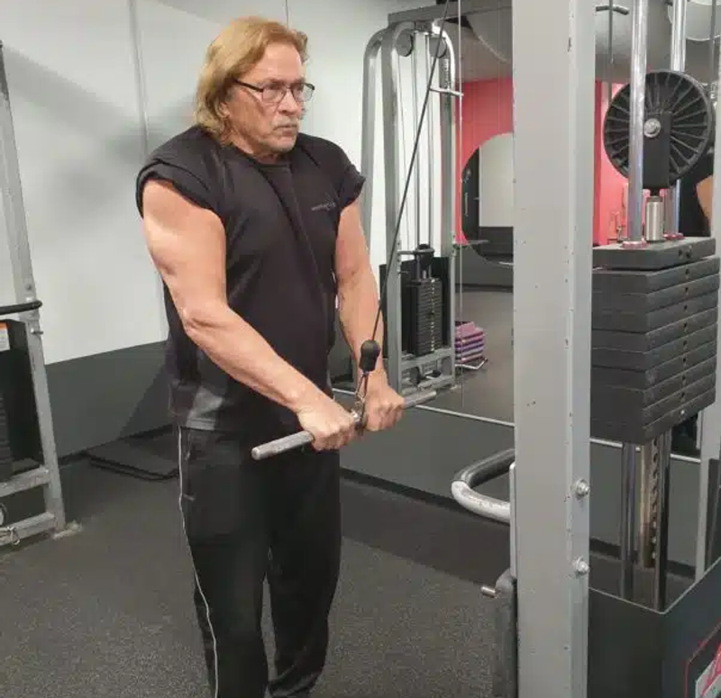 68 year old man in a gym doing pulldowns flexing his triseps