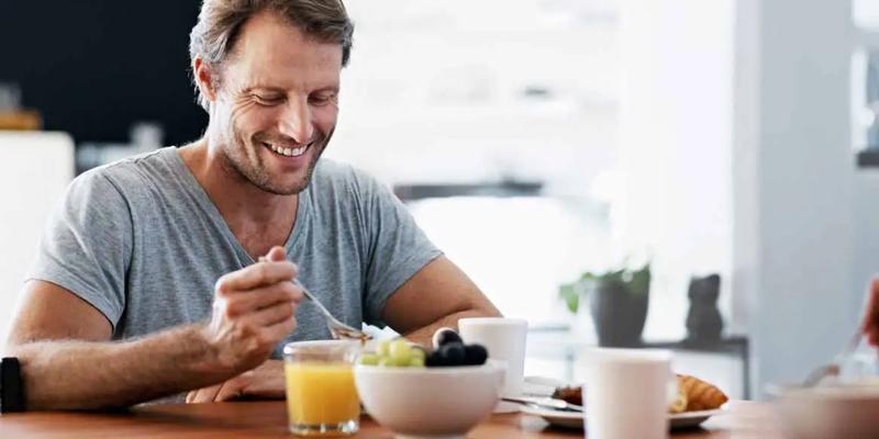 Mann som spiser sunn frokost for prostata, med frukt og juice