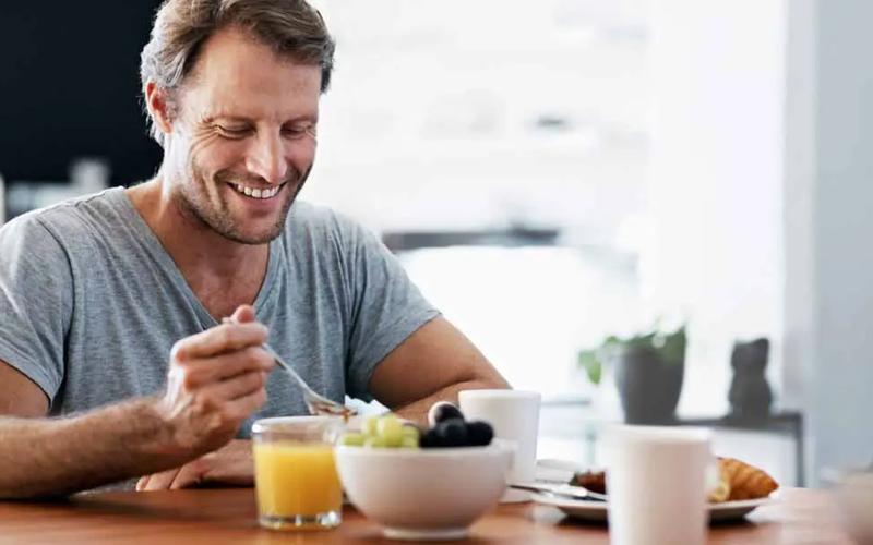 Mann som spiser sunn frokost for prostata, med frukt og juice