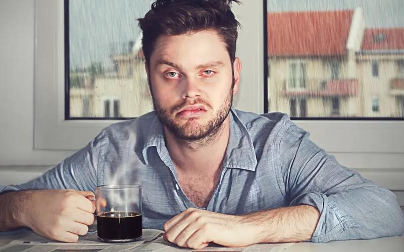 Trøtt mann som drikker kaffe og ser sur ut