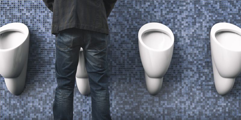 Mand der står med ryggen til og tisser, på et urinal.