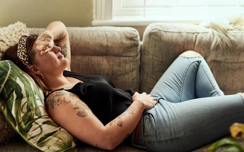 Kvinne som ligger på sofaen med PMS-ubehag