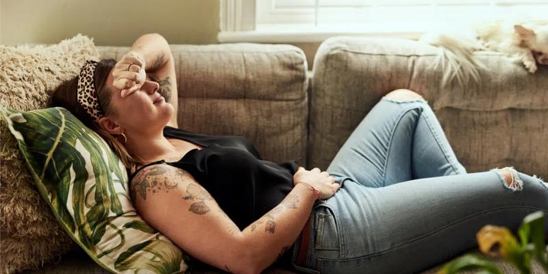 Kvinna som ligger på soffan med PMS-besvär