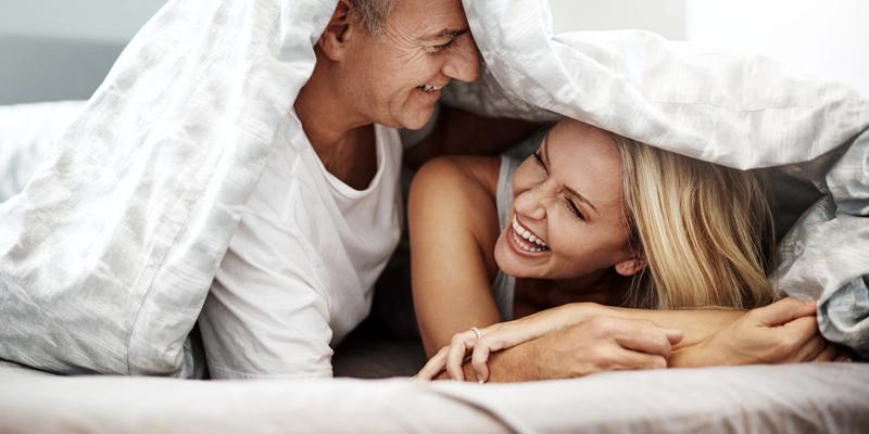 Par med god sexlust som flirtar och skrattar under täcket