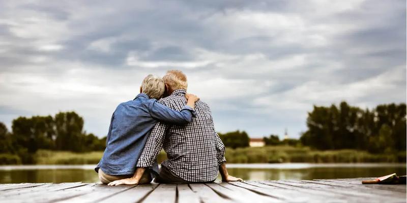 Ældre par som sidder på en bro og omfavner hinanden