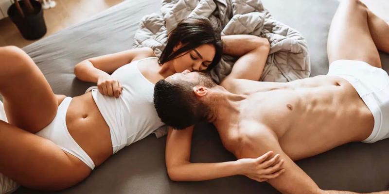 Mies ja nainen suutelevat sängyllä alusvaatteissa