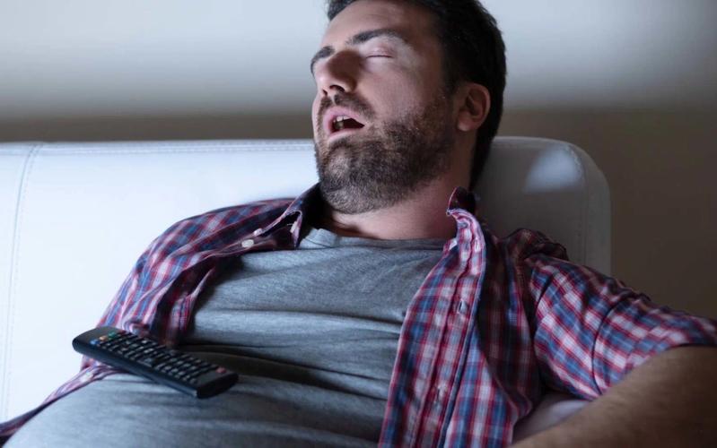 Mand uden energi som er faldet i søvn på sofaen foran fjernsynet