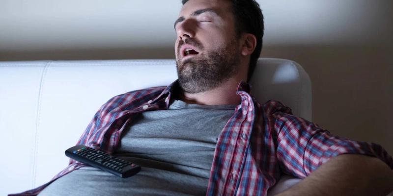 Mand uden energi som er faldet i søvn på sofaen foran fjernsynet