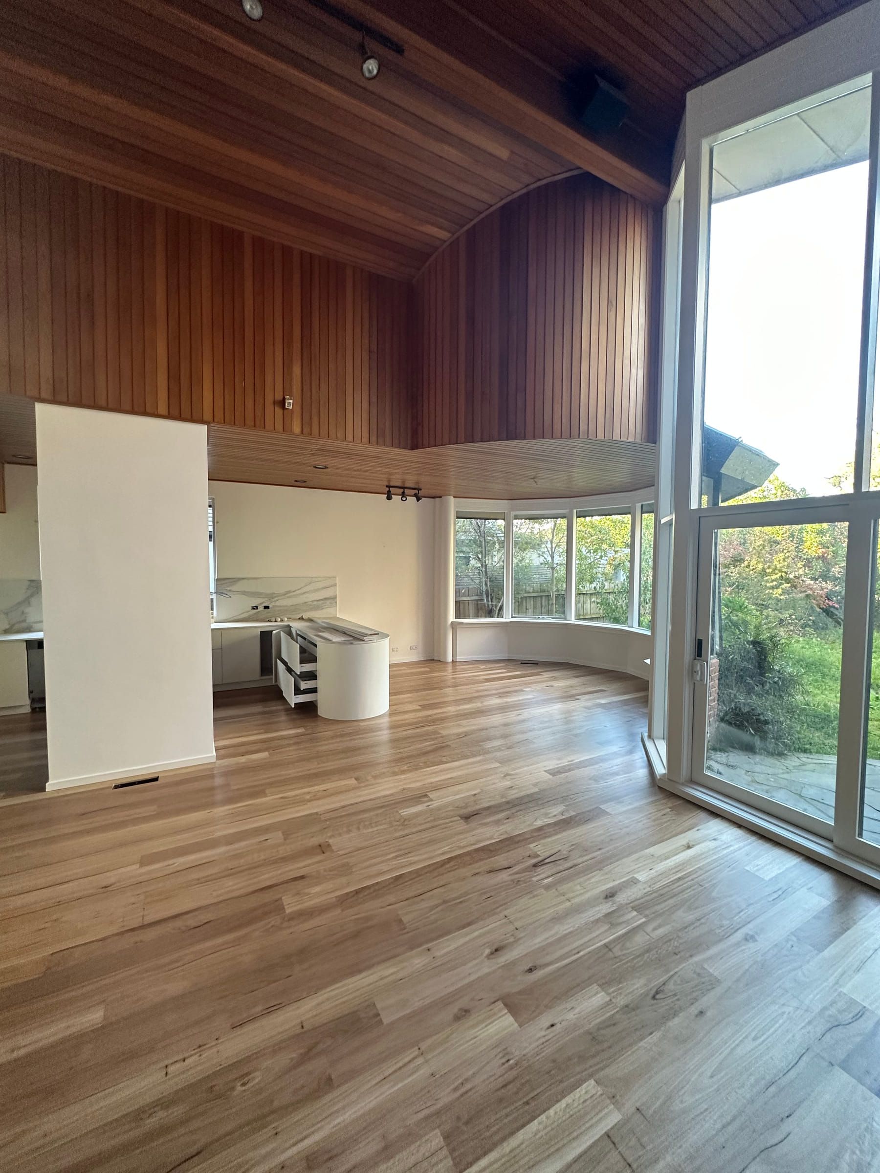Polished solid Blackbutt flooring beneath a double-height timber ceiling and tall windows.