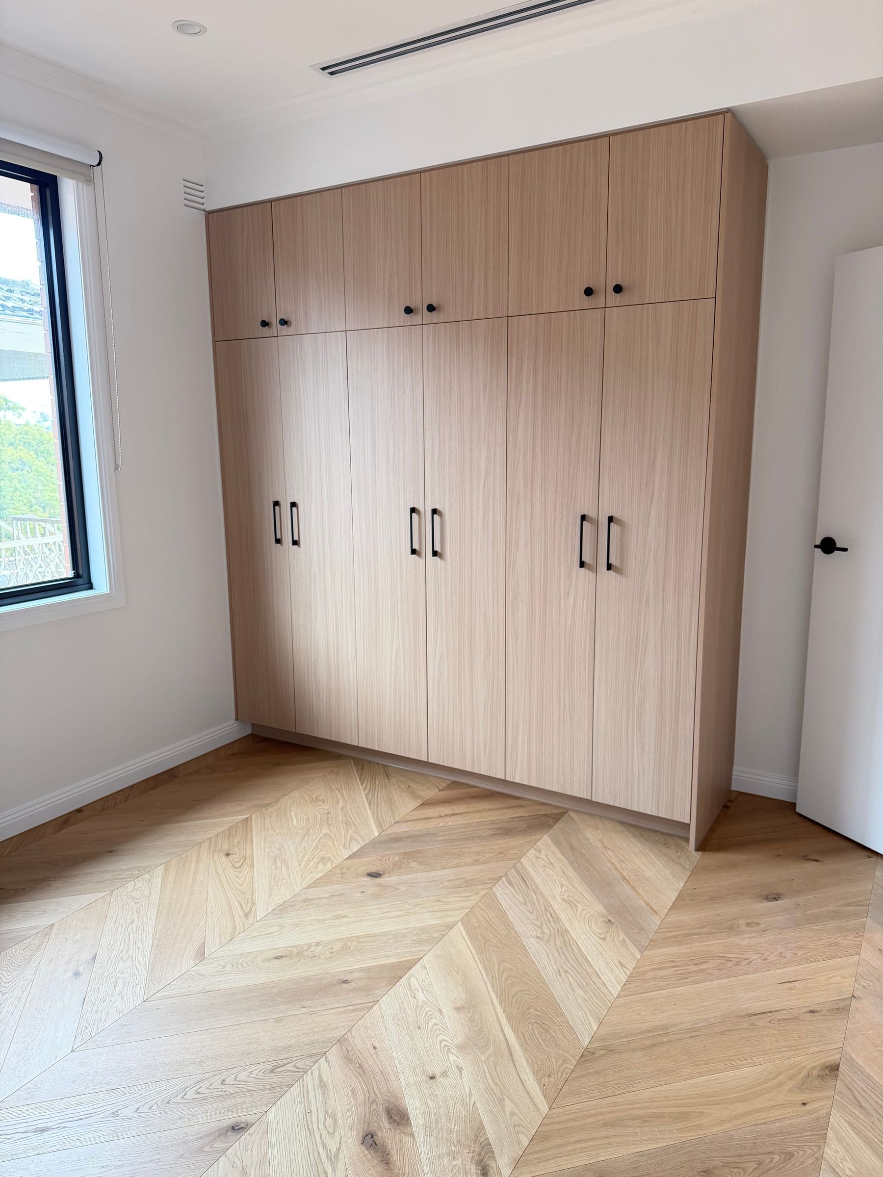 Natural Oak chevron floor beside full-height built-in wardrobes in a Bulleen bedroom.