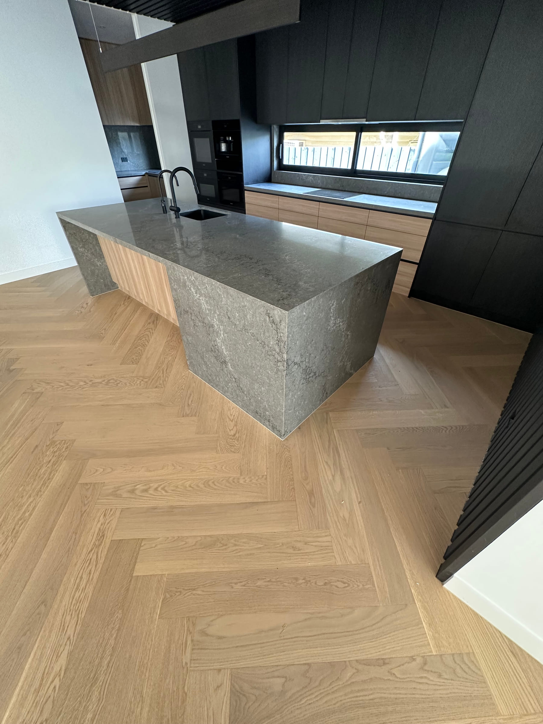 Natural herringbone flooring surrounding a stone kitchen island in a Camberwell home.