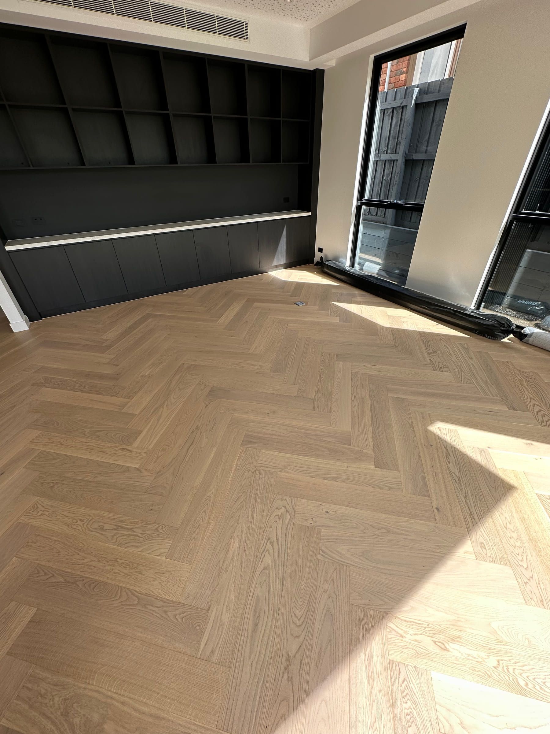 Natural oak herringbone flooring in a sunlit Camberwell room with dark cabinetry.