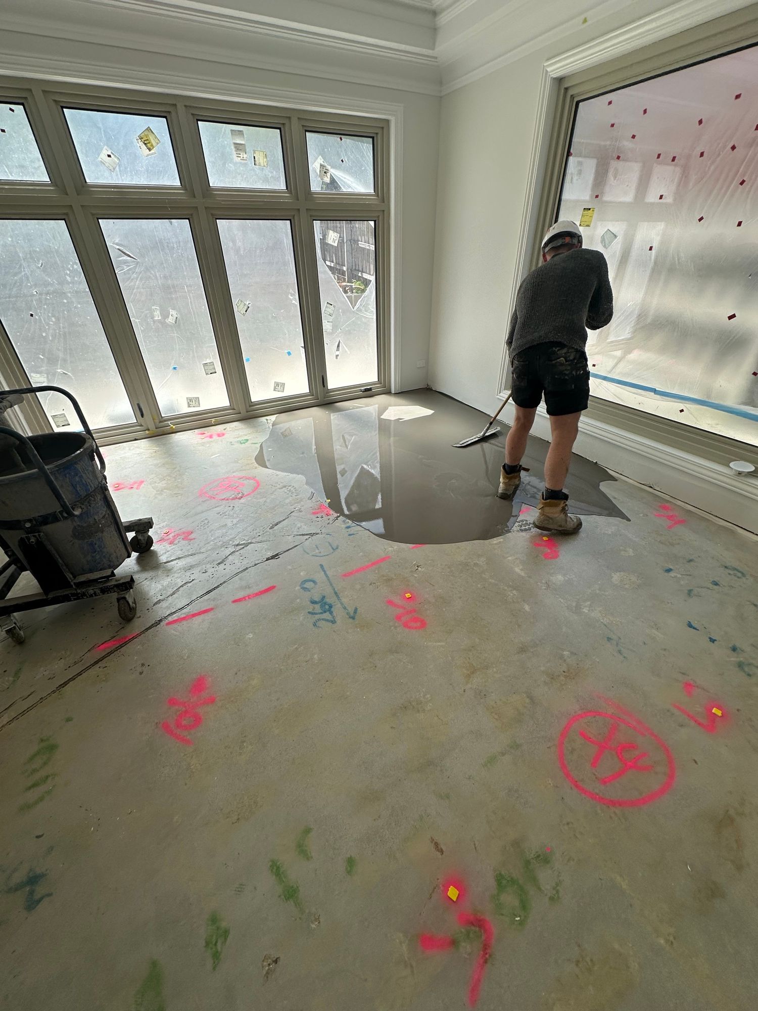 Flooring installer spreading self-levelling compound across a prepared residential concrete subfloor.