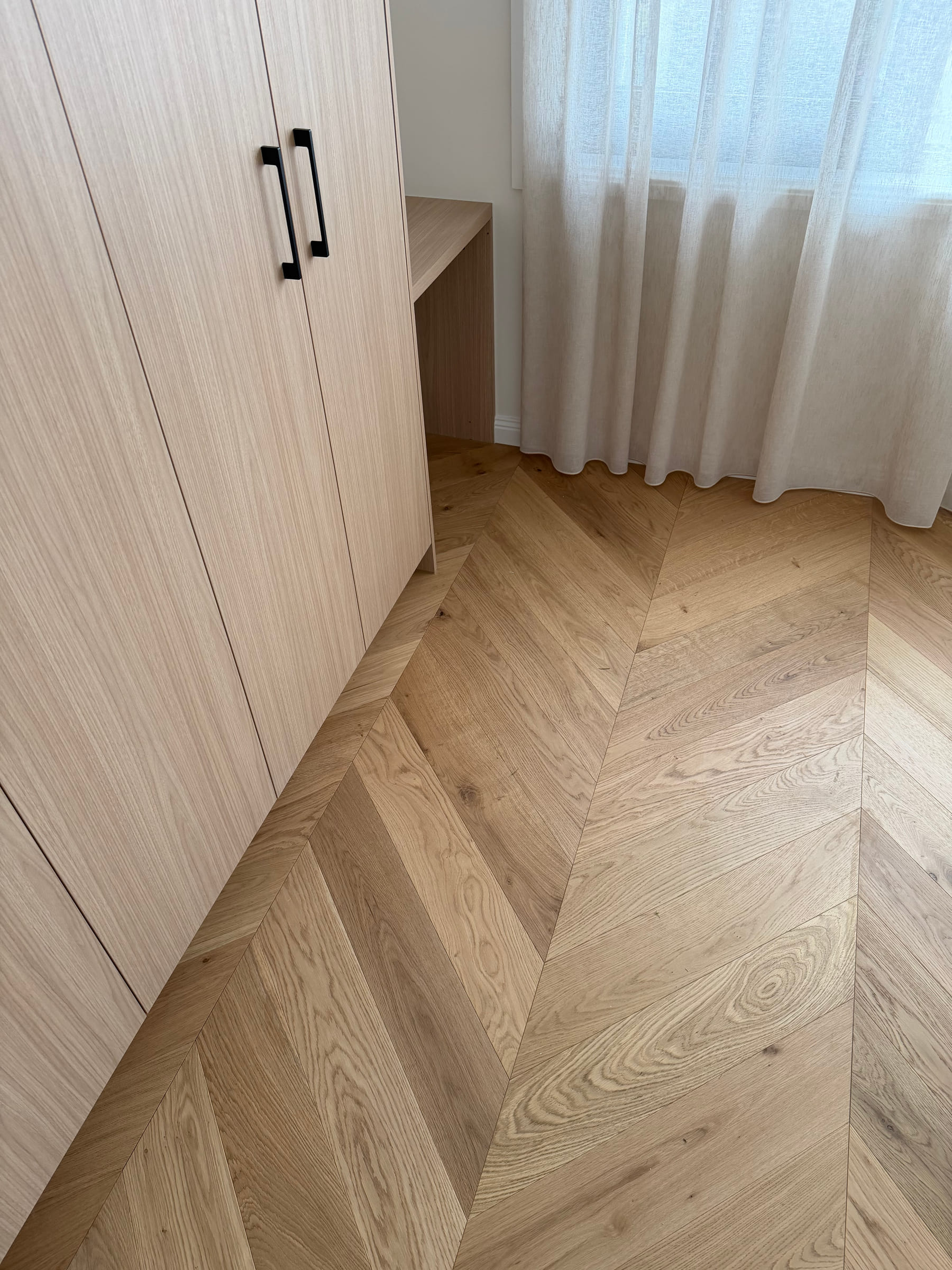 Natural Oak chevron flooring beside pale timber wardrobes and full-height curtains in a Bulleen bedroom.
