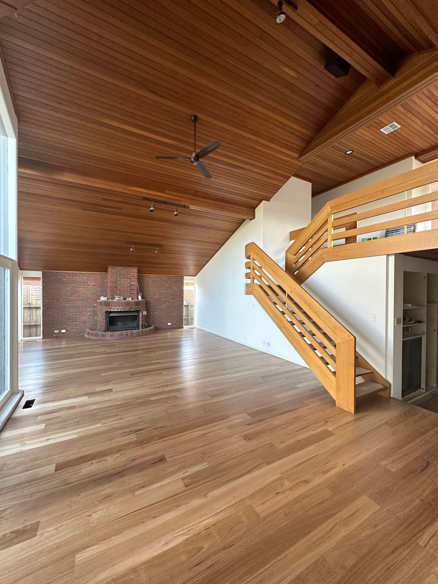 Blackbutt timber flooring across an open-plan living room with a staircase and brick fireplace.