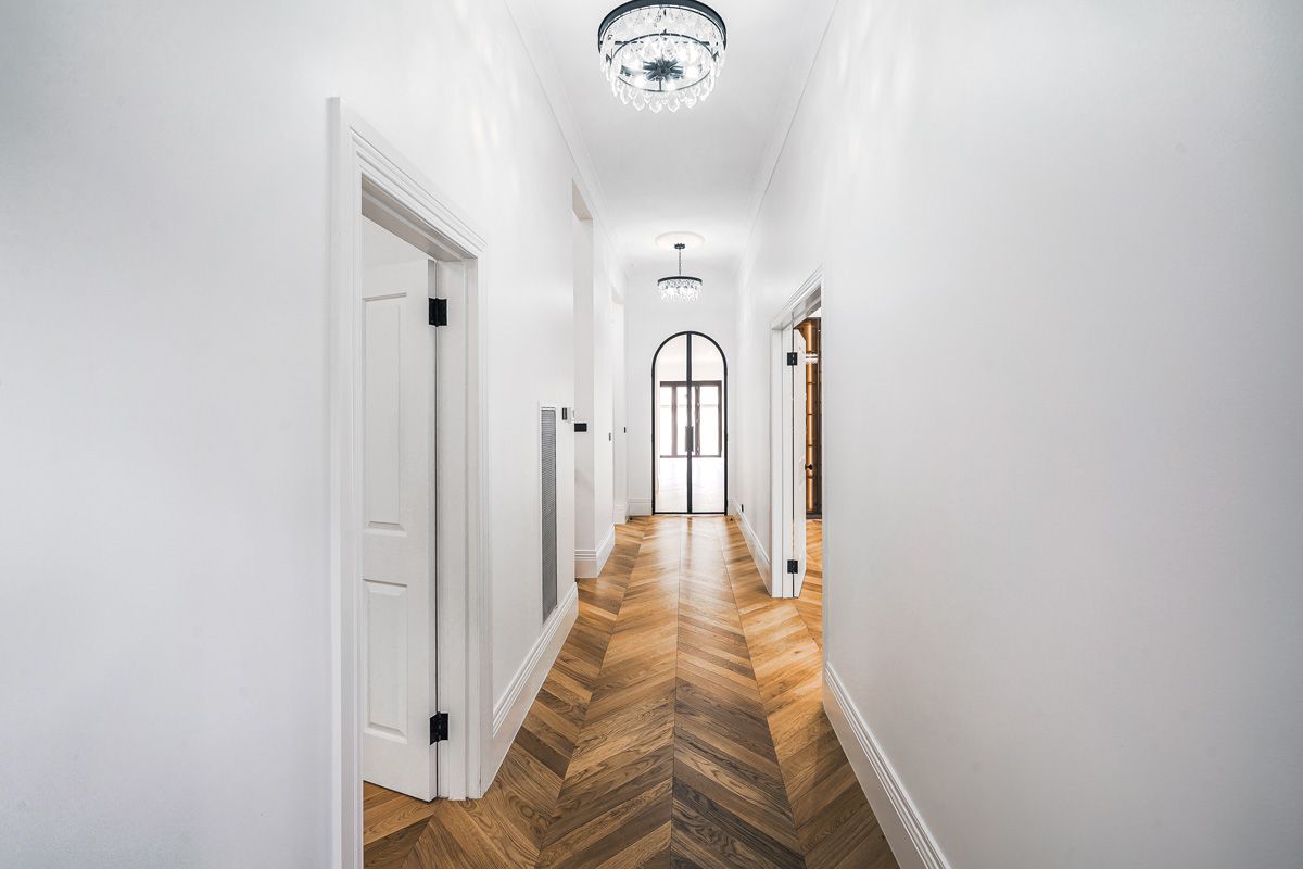 Chevron flooring aligned along a Kew hallway towards an arched steel-framed door.