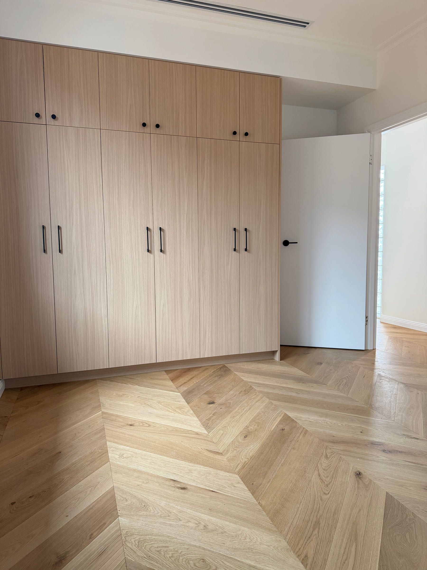 Chevron oak flooring set out around built-in bedroom joinery and a doorway in Bulleen.