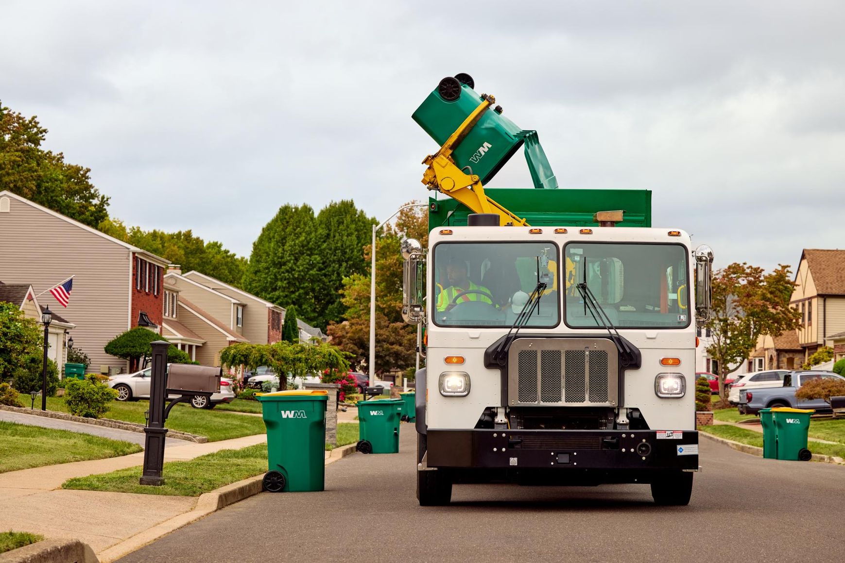 A garbage truck empties a green bin on a residential street.