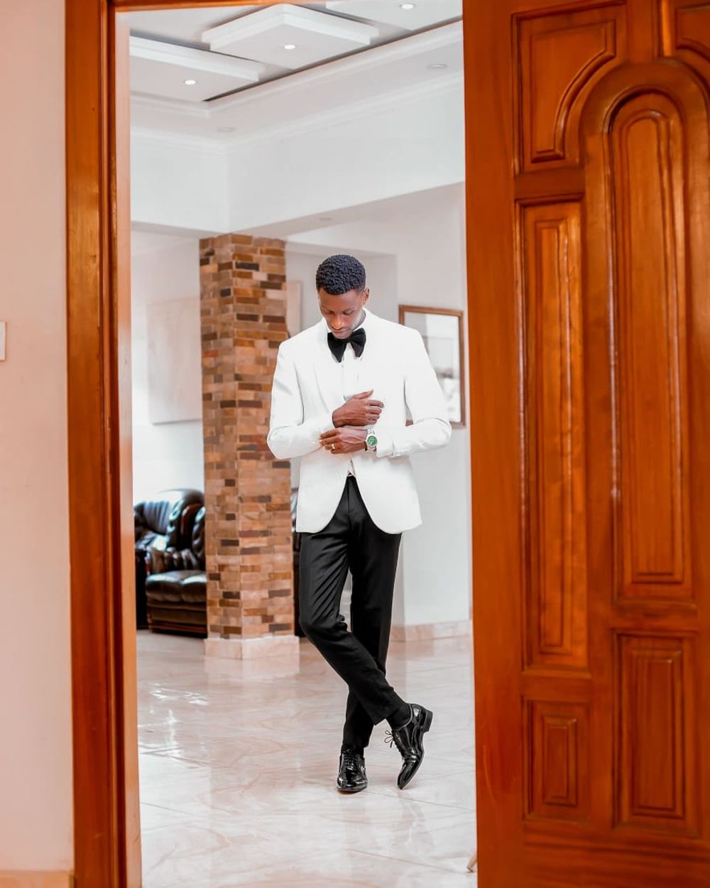 Groom in a white tuxedo walking through a doorway before the ceremony