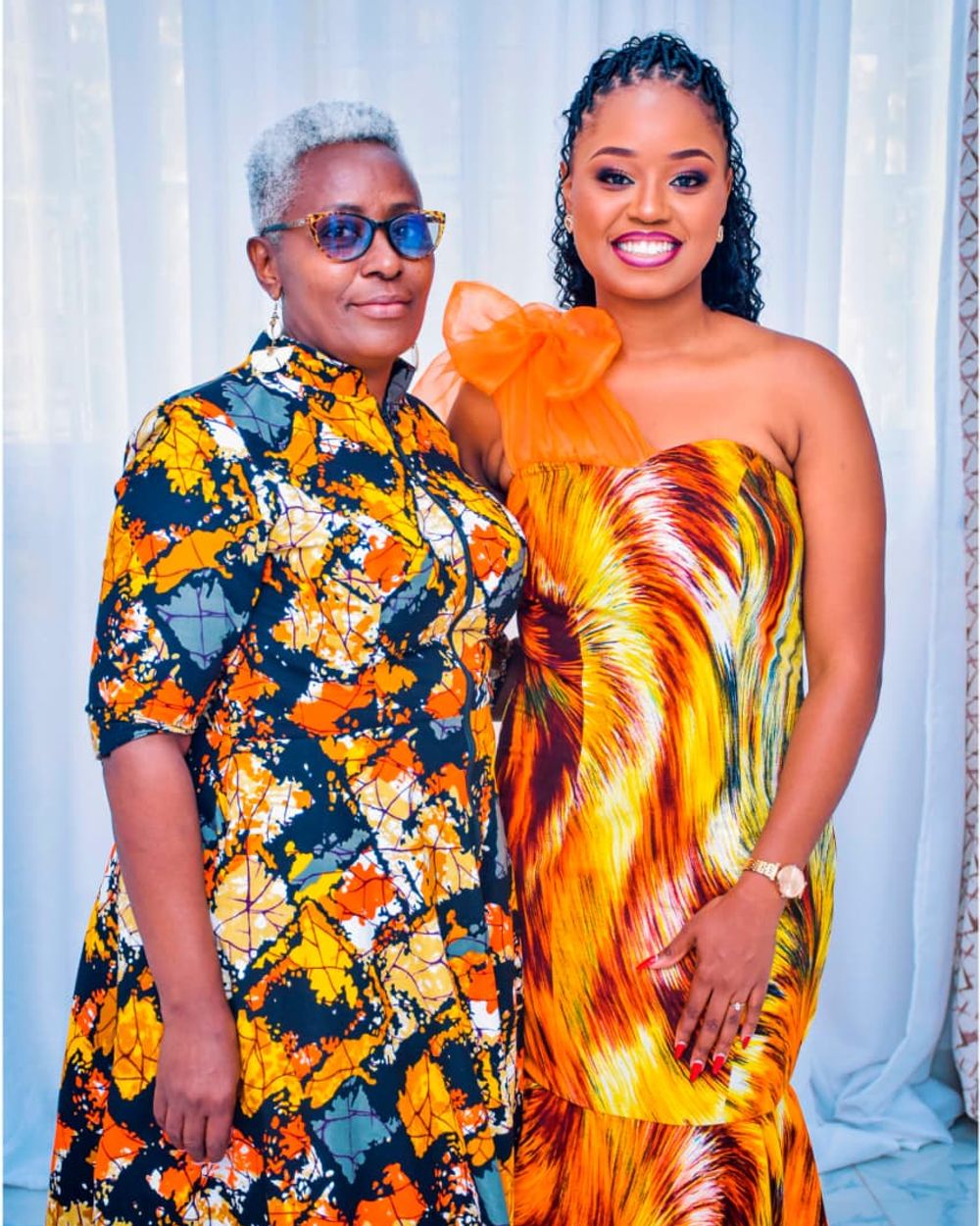 Two women in matching orange and gold outfits posing together for a studio portrait