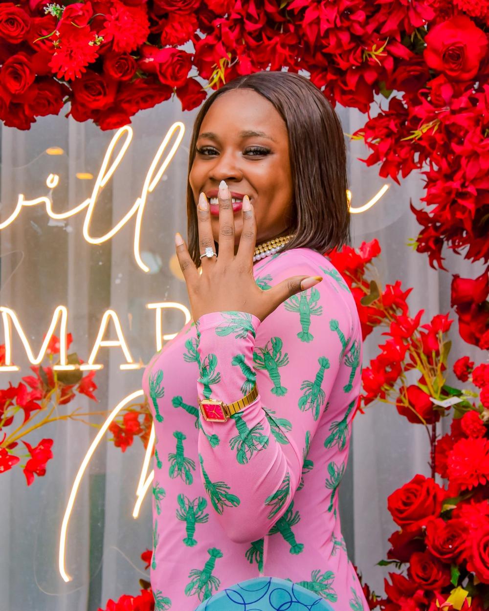 Woman showing off her engagement ring in front of the rose arch