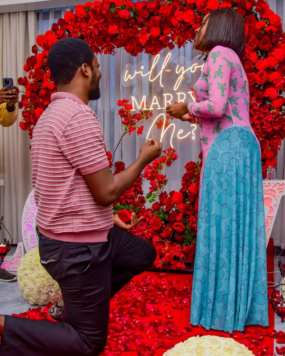 Man kneeling to propose with a ring in front of a rose arch