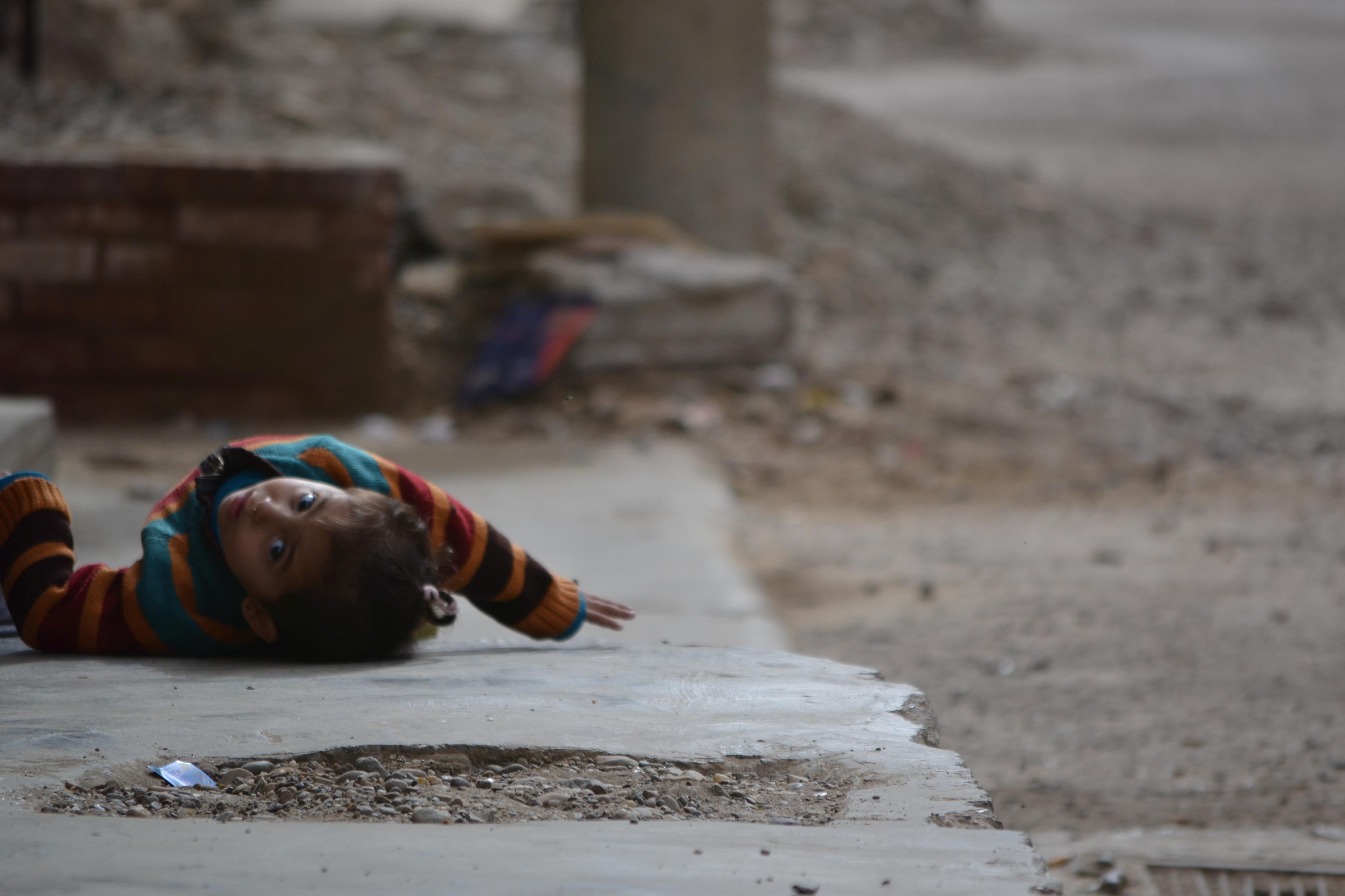 Une petite fille luttant contre la chaleur en s'allongeant dans la rue à côté de sa maison