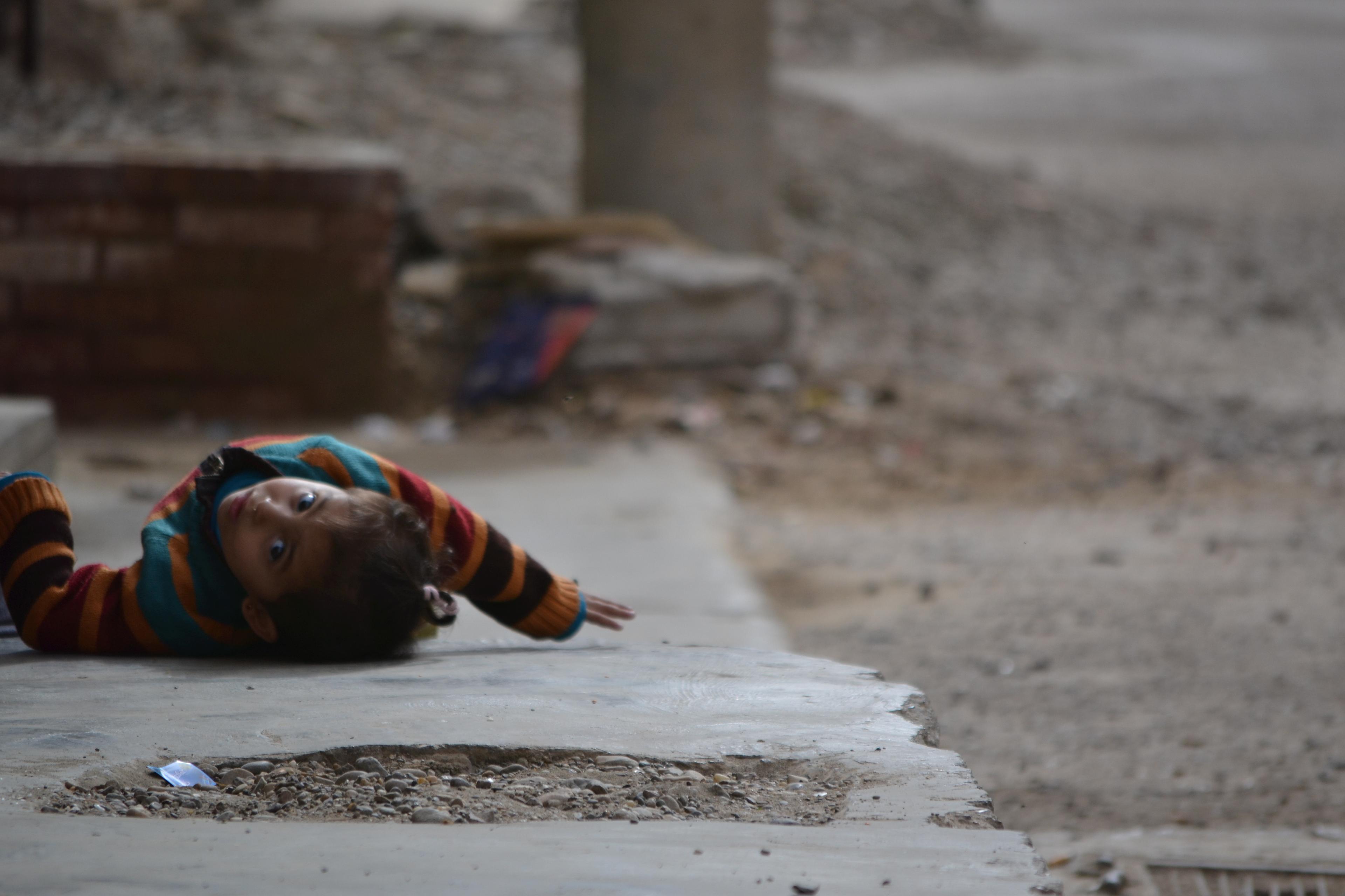 A little girl fighting the heat by laying down on the street next to her home