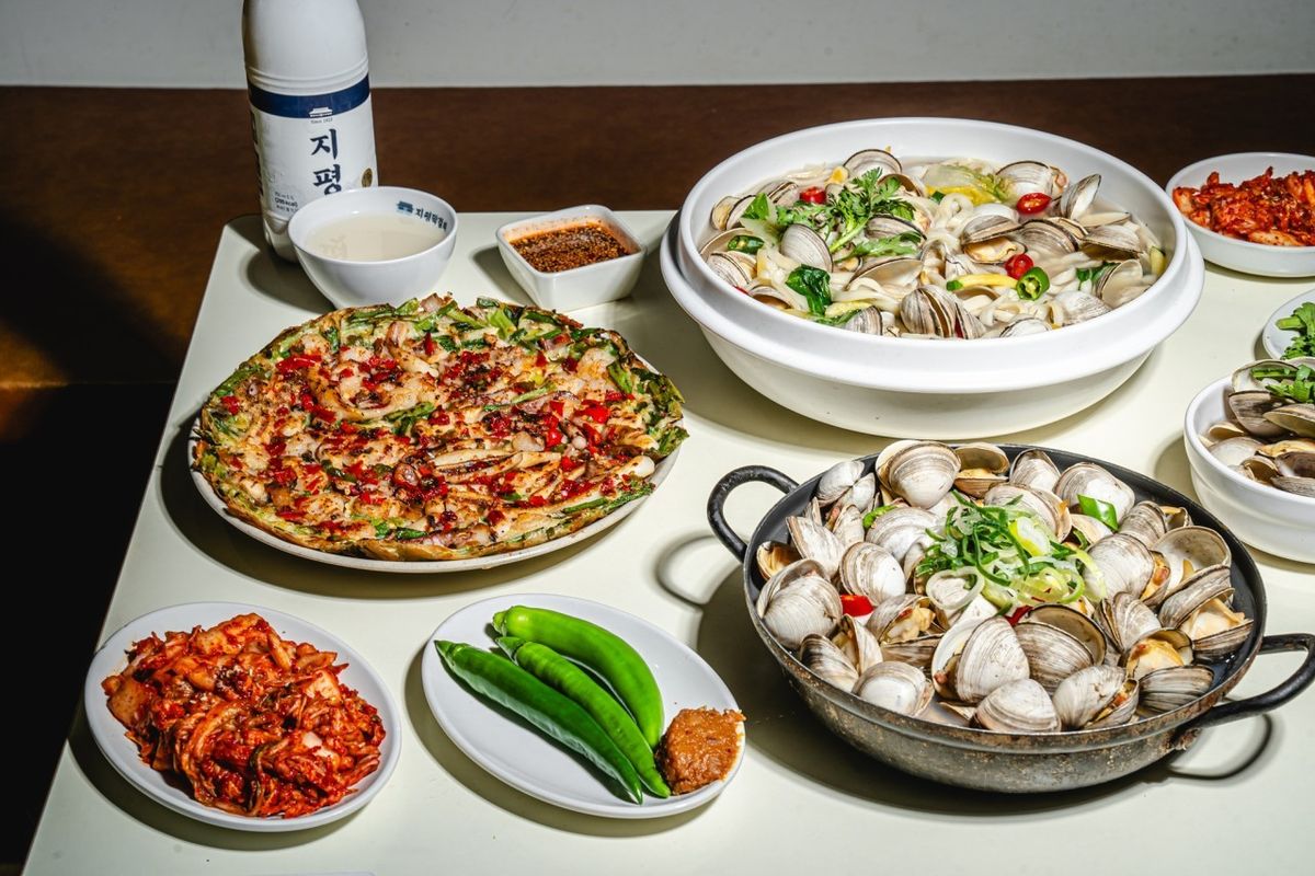 A spread at JoJo Kalguksu: clam knife-cut noodles, a pan of steamed clams, a seafood pancake, kimchi, and makgeolli.
