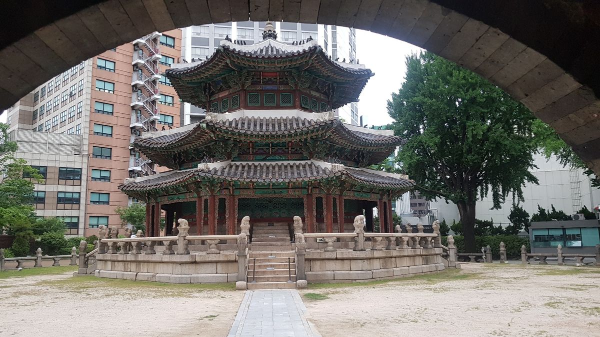 The octagonal Hwangungu shrine, a three-tiered pavilion with painted traditional eaves, standing among modern high-rise buildings near Seoul City Hall.